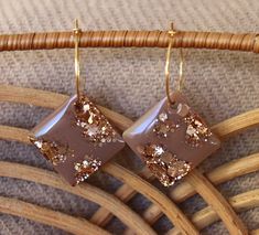 a pair of brown and gold earrings sitting on top of a wooden chair next to a wicker basket