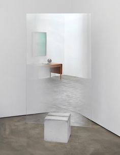 an empty room with white walls and a small table in the corner, as well as a mirror on the wall