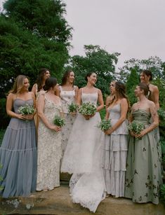 a group of women standing next to each other wearing dresses and holding bouquets in their hands