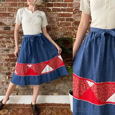 a woman standing next to a brick wall wearing a blue skirt with red and white designs