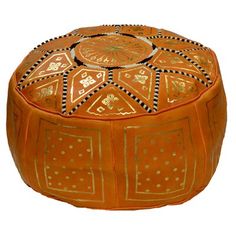 an orange ottoman with gold and black designs on the top, sitting in front of a white background