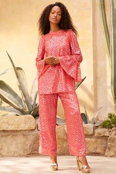 a woman standing in front of a cactus plant wearing pink sequin pants and top