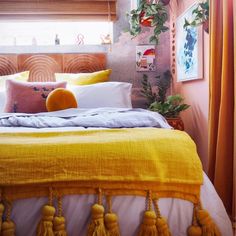 a bed with yellow linens and pillows in a bedroom next to potted plants