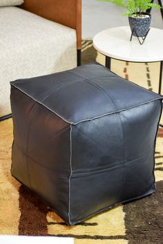 a black leather ottoman sitting on top of a rug next to a chair and table