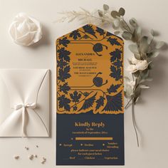 an orange and black wedding card on top of a white envelope next to some flowers