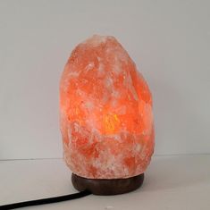 an orange himalayan salt lamp sitting on top of a wooden stand next to a white wall