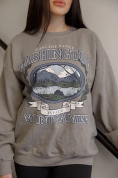 Experience the beauty of nature with our Washington Mount Rainier sweatshirt. Inspired by vintage designs, this graphic sweatshirt showcases the majestic Mount Rainier in soft shades of grey. Perfect for outdoor enthusiasts and fashion lovers alike. distressed vintage inspired graphic long sleeves crew neck relaxed fit model is wearing a s/m Casual Outdoor Sweatshirt With Screen Print, Casual Outdoor Screen Print Sweatshirt, Gray Cotton Outdoor Sweatshirt, Gray Tops For Outdoor Activities In Fall, Gray Tops For Fall Outdoor Activities, Fall Hiking Sweatshirt Crew Neck, Fall Hiking Crew Neck Sweatshirt, Fall Crew Neck Sweatshirt For Hiking, Gray Sweatshirt For Outdoor Fall Activities