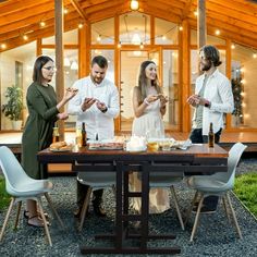 four people standing around a table with food and drinks in front of a house at night