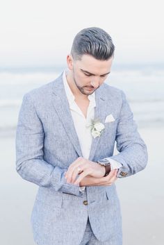 a man in a gray suit and white flower boutonniere looks down at his watch