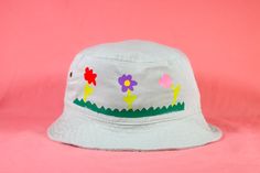 Level up your flower power with this cute bucket hat. What are these hats made of?‣ Hats are 100% cotton and have 4 brass eyelets for ventilation.‣ The head measurement of this hat is about 23 inches.How are these hats made?‣ Designs are applied with heat transfer vinyl.‣ I embellish each hat by hand, so please allow for slight variations from the photos. This just means that there is no hat exactly like yours. :)‣ Colors may vary slightly due to monitor or screen differences. For shipping infor Whimsical Cotton Hats For Spring, Playful Green Sun Hat For Spring, Playful Cotton Sun Hat For Spring, Cute Cotton Bucket Hat For Summer, Whimsical Bucket Hat With Curved Brim For Spring, Playful Bucket Hat For Spring Festival, Fun Cotton Hats For Spring, Cute Cotton Sun Hat For Spring, Fun Bucket Hat For Spring