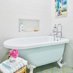 a bathroom with a claw foot tub and blue tile flooring, along with a pink flower on the side of the bathtub