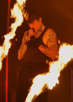 a man with tattoos holding a microphone in front of some bright flames on a stage