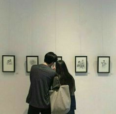 a man and woman standing next to each other looking at pictures on the wall