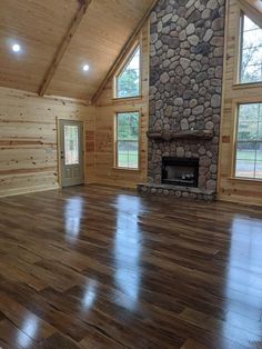 an empty living room with wood floors and stone fireplace in the center, surrounded by large windows