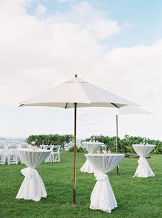 an outdoor wedding setup with white linens and tablecloths on the grass under an umbrella