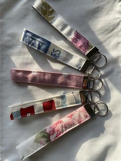 four keychains with different designs on them sitting on a white cloth covered surface