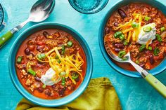 two bowls of chili and beans with sour cream on top, next to spoons