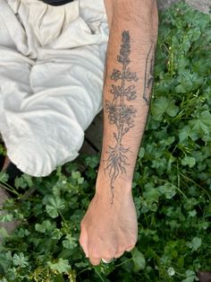 a man with tattoos on his arm sitting in front of some green plants and weeds