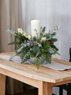 a wooden table topped with a white candle next to a vase filled with flowers and greenery