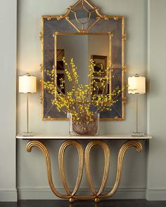 an ornate console table with a mirror above it and flowers in a vase on top