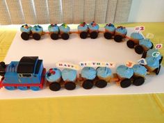 a birthday cake shaped like a train with cupcakes on the tracks and numbers