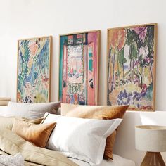 three paintings hang on the wall above a bed with white sheets and pillows, along with two lamps