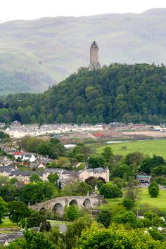 the town is surrounded by mountains and trees, with a clock tower in the distance