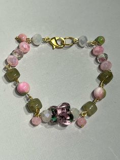 Gorgeous glass beads make up this bracelet and give it a cohesive yet unique feel as the pink and green colors reflect the design inside the butterfly and white beads. Those beads feature pink flowers with green leaves inlaid with the white having gold streaks as well. Beautifully soft bracelet gives the feel of a forest fairy or a perfect accessory for a tea party.  Durable beads and connections make this bracelet perfect for everyday  or heavy use. May break under extreme unintended use.  Made to fit. For Reference, the bracelet in the photo is 7.5 inches long and is standard size, smaller wrist chose 7 inches to ensure snug fit. Male standard size is 8 inches.  Larger sizes will have bead pattern repeated until desired length.  Each item bought will be set with an assortment of freebies Pink Flower Glass Jewelry, Pink Flower-shaped Glass Jewelry, Pink Crystal Bracelet With Large Beads For Gift, Pink Crystal Bracelet With Large Beads As Gift, Pink Glass Jewelry With Faceted Beads, Adjustable Pink Glass Bracelets, Adjustable Pink Bracelets, Pink Glass Beaded Bracelets As Gift, Green Glass Bracelets With Colorful Beads