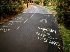 the chalk drawing on the road says keep calm and keep your distance written in cursive writing