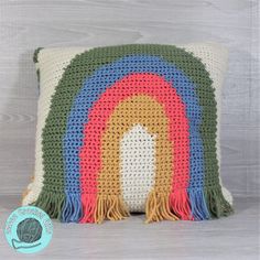 a crocheted pillow with a rainbow on the front and fringes around it