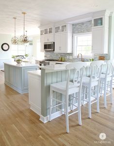 a large kitchen with white cabinets and counter tops, along with bar stools that match the hardwood flooring