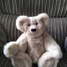 a white teddy bear sitting on top of a gray couch next to a black and white striped wall