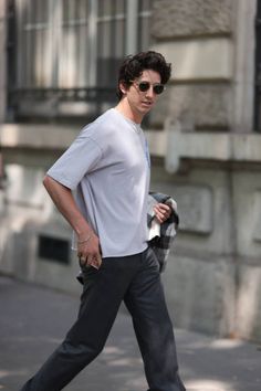 a man in white shirt and black pants walking down the street with his hand on his hip