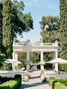 an outdoor wedding venue with white tables and umbrellas on the walkway between two rows of trees