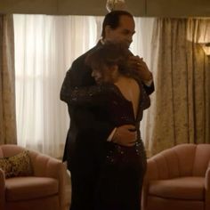 a man and woman standing in a living room next to each other with their arms around each other