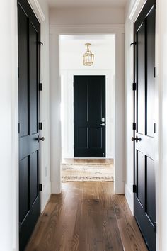 an empty hallway with black doors and wood flooring on either side of the door