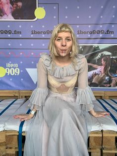 a woman sitting on top of a bed with her hands in her mouth while making a funny face