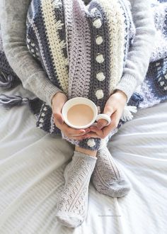 a woman holding a cup of coffee on top of a bed