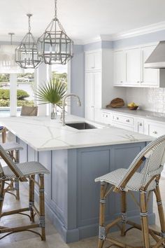 a kitchen with blue and white cabinets, an island countertop and two stools in front of the sink