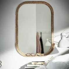 a mirror sitting on top of a table next to a lamp and a white bed