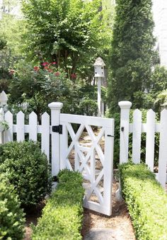 a white picket fence surrounded by bushes and shrubs with a lantern on the top one