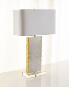 a marble lamp on a white table with a gray shade over the base and a gold trim around it