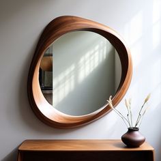 a round mirror sitting on top of a wooden table next to a vase with flowers