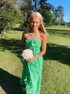 a young woman in a green dress holding a white flower and posing for the camera