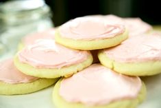 pink frosted cookies on a white plate with a jar of water in the background