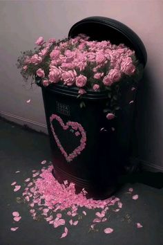 a trash can filled with pink flowers and petals on the floor next to a wall