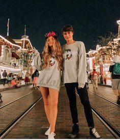 a man and woman standing next to each other in front of christmas lights at night