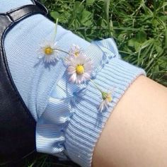 a woman's arm with daisies on it and her shoes in the grass