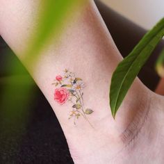 a small flower tattoo on the foot of a woman's left ankle with green leaves