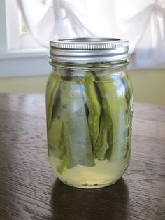 a jar filled with pickles sitting on top of a wooden table next to a window